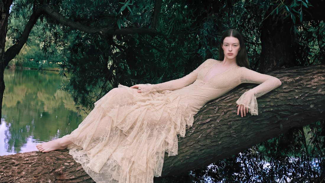 Model in a lace gown reclining on a tree trunk beside a lake